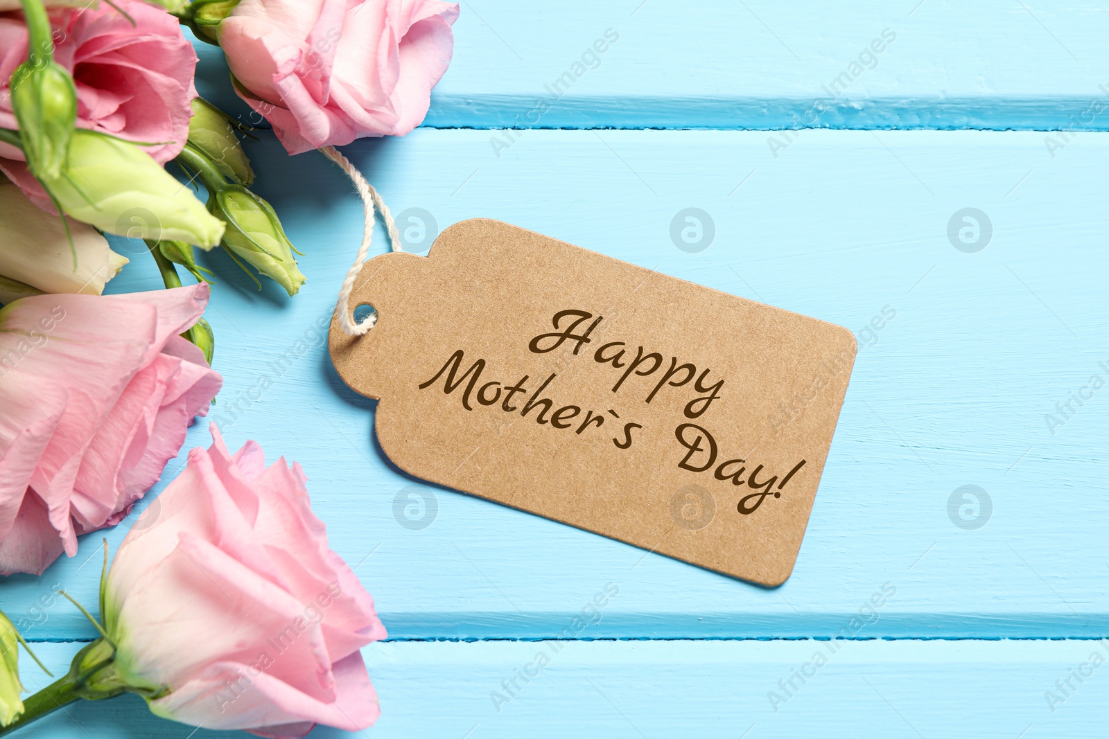 Image of Happy Mother's Day greeting label and beautiful flowers on light blue wooden table