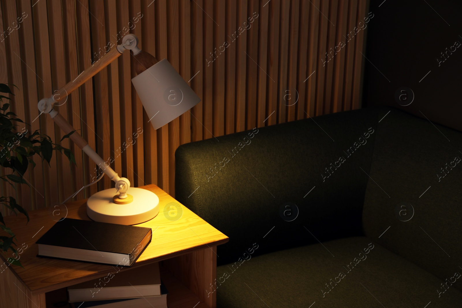 Photo of Stylish modern desk lamp and book on wooden cabinet in living room