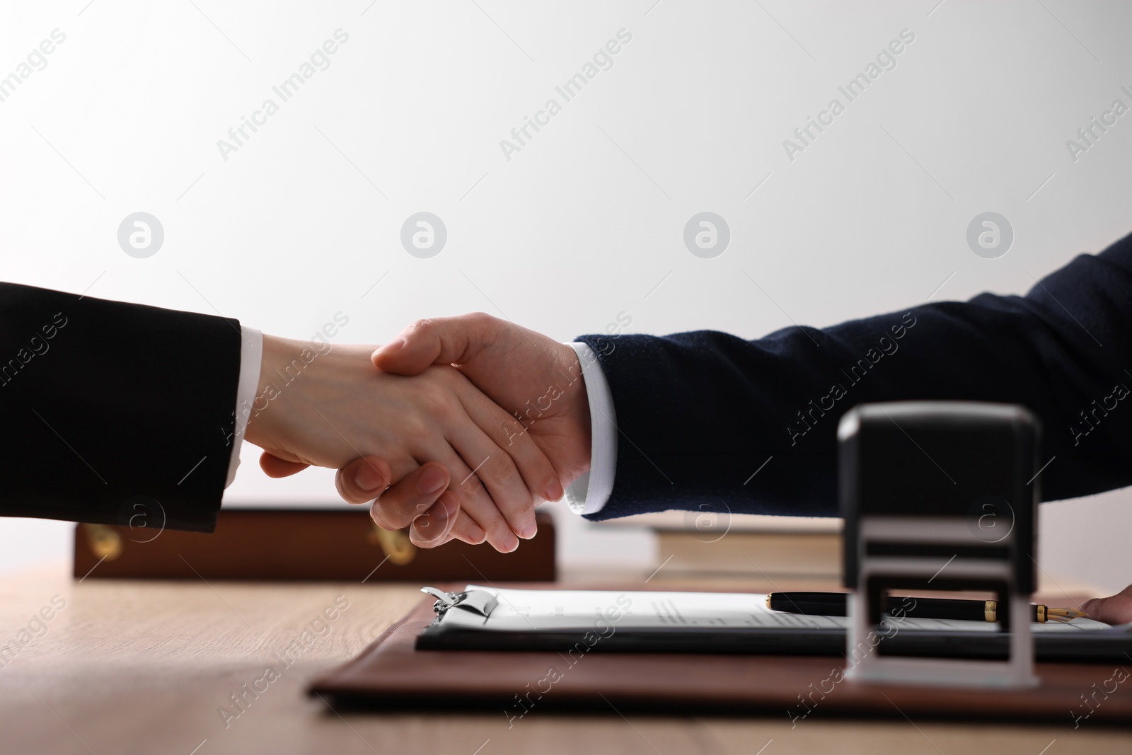 Photo of Notary shaking hands with client at wooden table in office, closeup