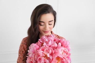 Beautiful young woman with bouquet of pink peonies on white background