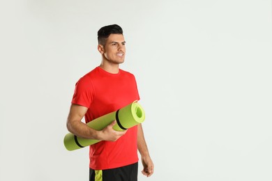 Photo of Handsome man with yoga mat on light background. Space for text