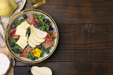 Tasty salad with brie cheese, prosciutto, blueberries and pear on wooden table, flat lay. Space for text