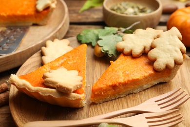 Slices of delicious homemade pumpkin pie on wooden plate, closeup