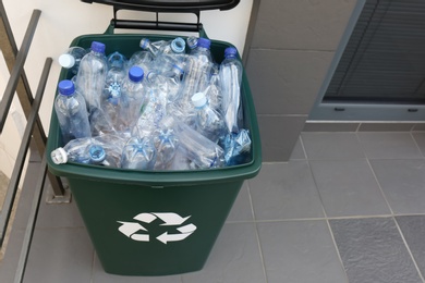 Photo of Many used plastic bottles in trash bin near entrance outdoors. Recycling problem