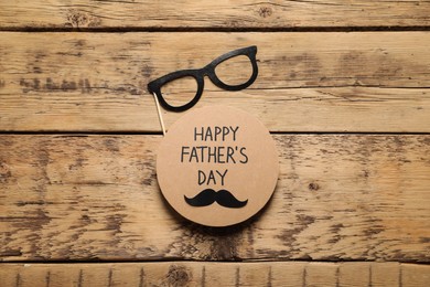 Photo of Card with phrase Happy Father's Day and paper glasses on wooden background, flat lay