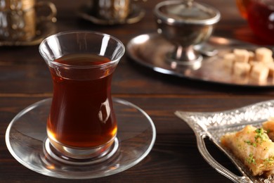 Photo of Traditional Turkish tea in glass and baklava on wooden table, closeup