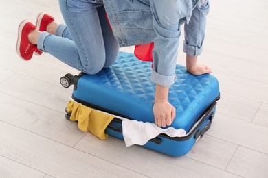 Photo of Young woman struggling to close suitcase indoors