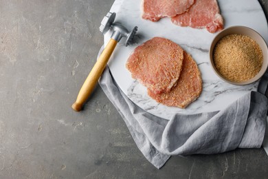 Photo of Cooking schnitzel. Raw pork chops, bread crumbs with meat mallet on grey table, top view and space for text