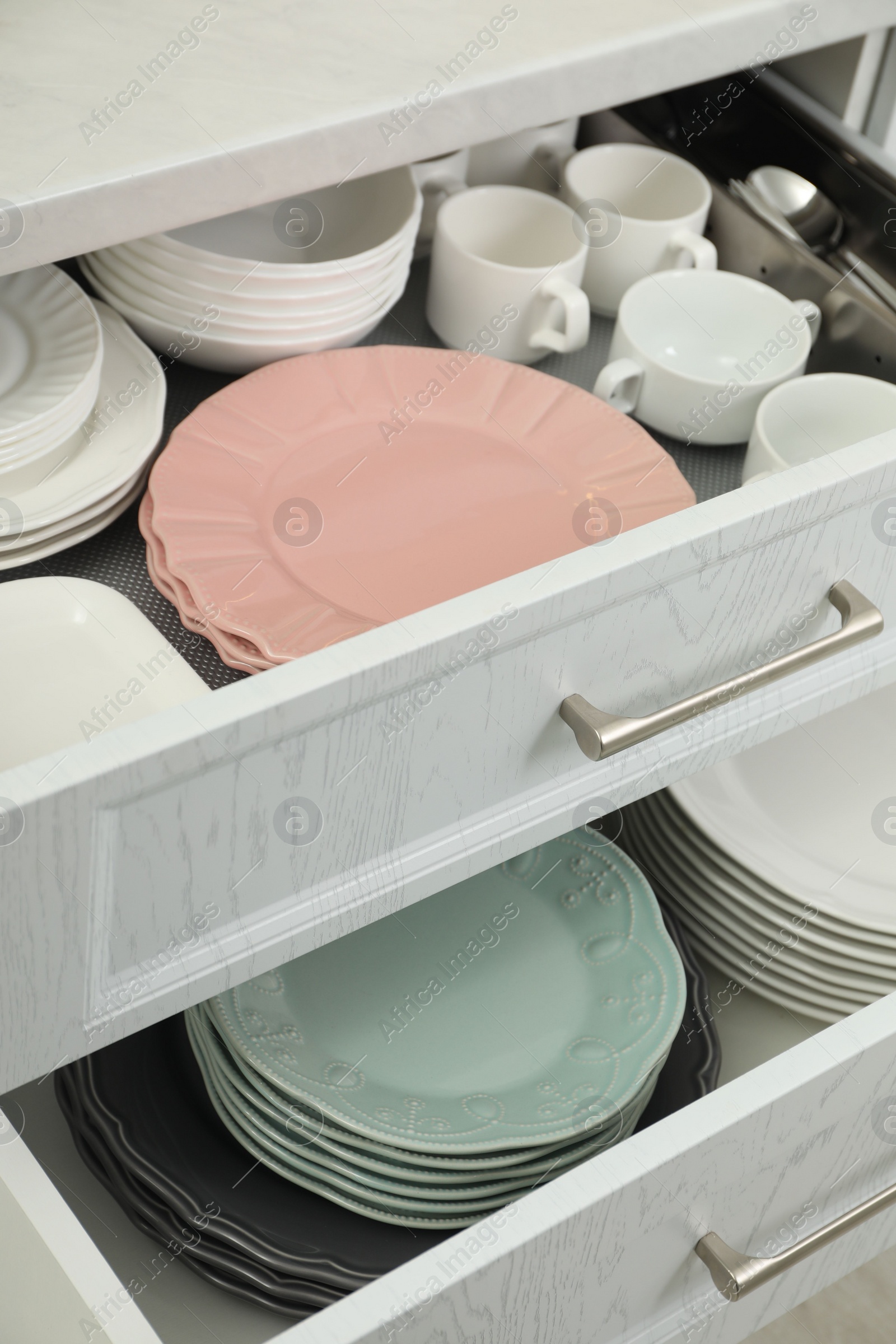 Photo of Clean plates, bowls and cups in drawers indoors