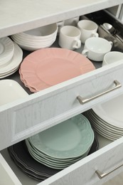 Photo of Clean plates, bowls and cups in drawers indoors