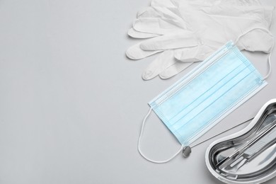 Photo of Set of different dentist's tools, face masks and gloves on light grey background, flat lay. Space for text