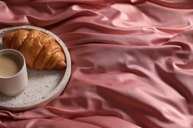 Tray with tasty croissant and cup of coffee on beautiful pink silk linens