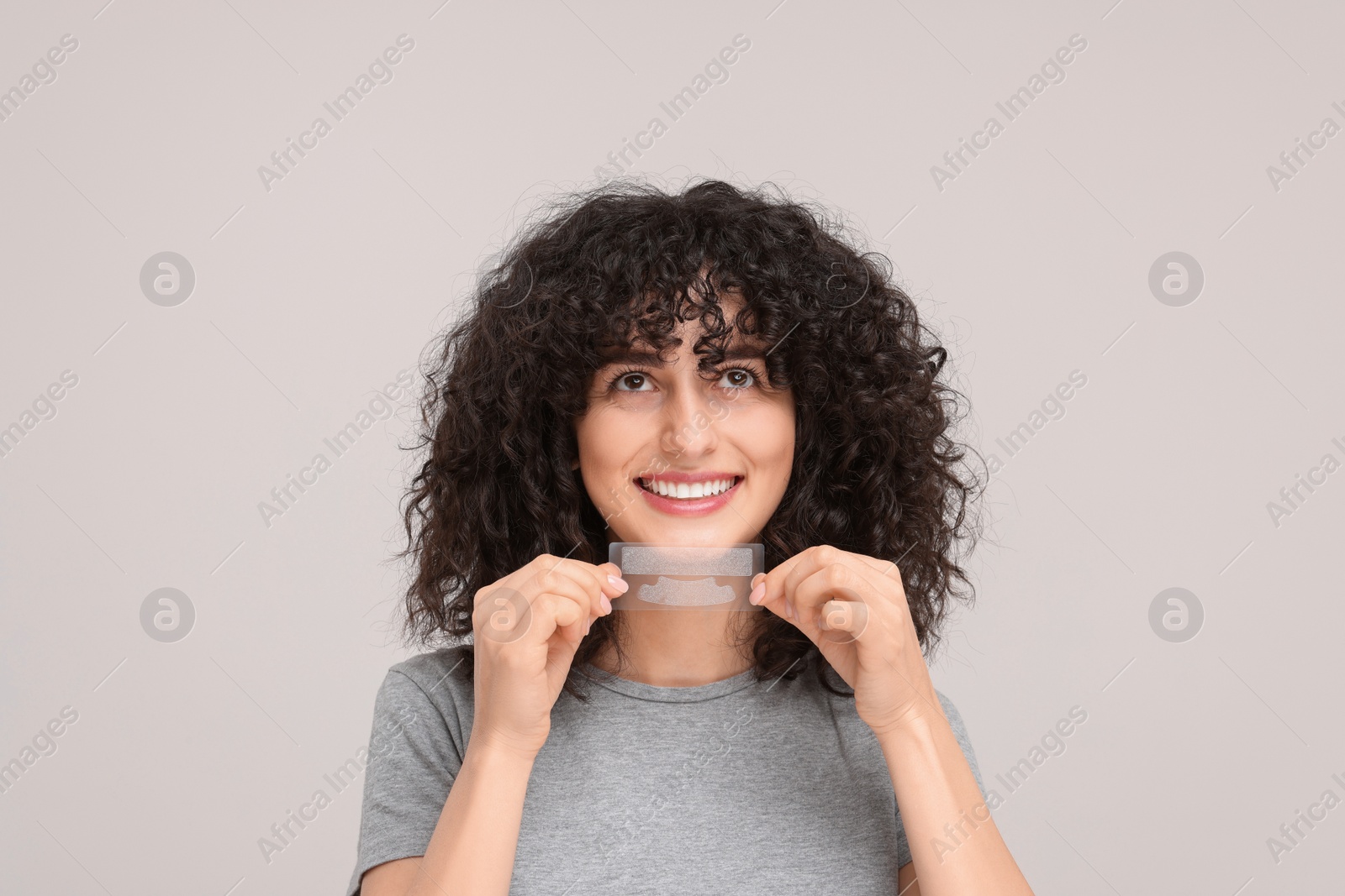 Photo of Young woman holding teeth whitening strips on light grey background