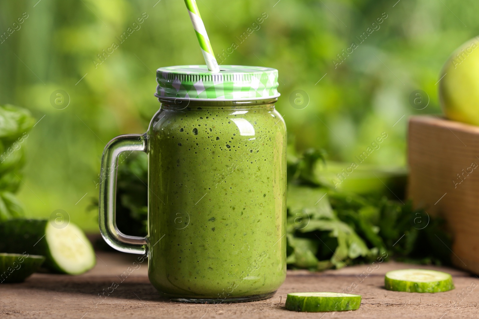 Photo of Mason jar of fresh green smoothie and ingredients on wooden table outdoors