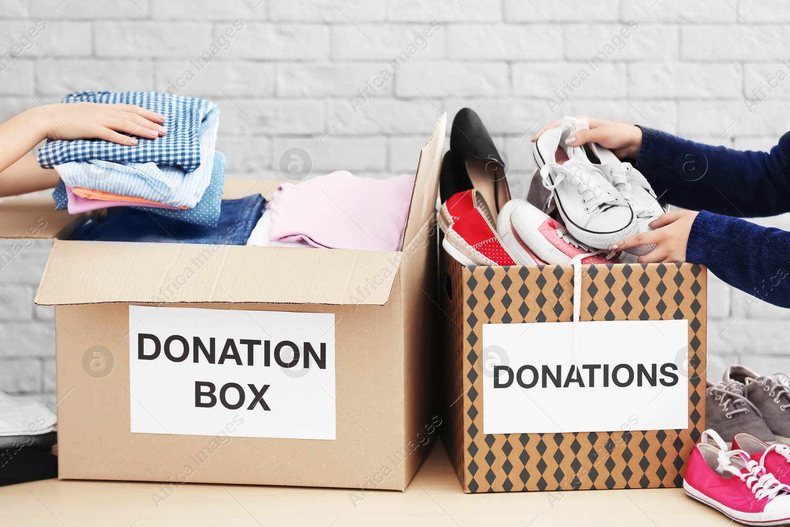 Photo of Female volunteers collecting clothes and shoes into donation boxes indoors