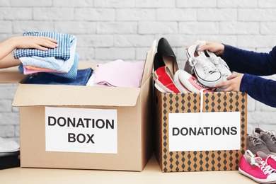 Photo of Female volunteers collecting clothes and shoes into donation boxes indoors