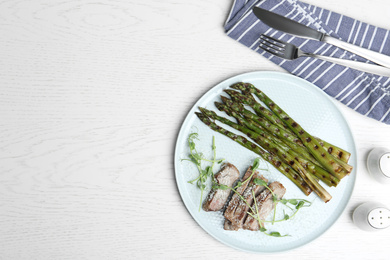 Photo of Tasty meat served with grilled asparagus on white wooden table, flat lay. Space for text