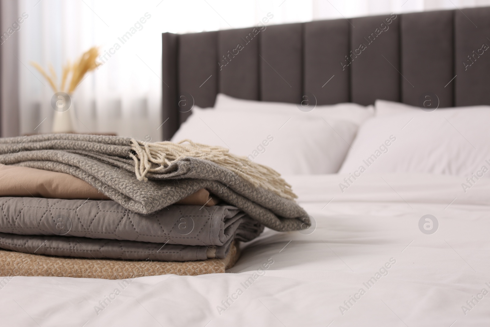 Photo of Stack of different folded blankets on bed in room, space for text. Home textile