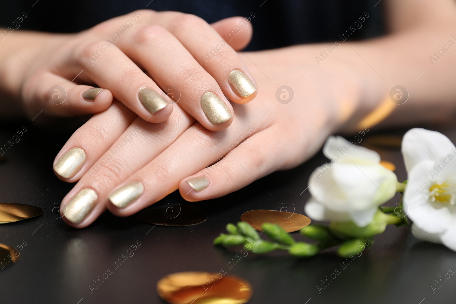 Photo of Woman with golden manicure on black table, closeup. Nail polish trends