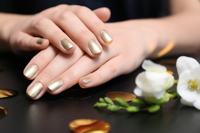 Photo of Woman with golden manicure on black table, closeup. Nail polish trends