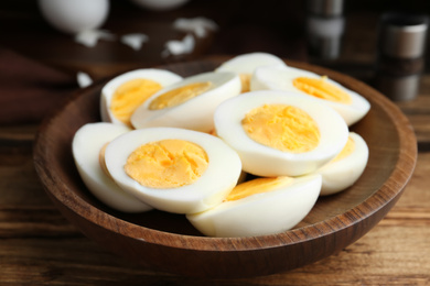 Photo of Cut hard boiled chicken eggs in wooden bowl on table