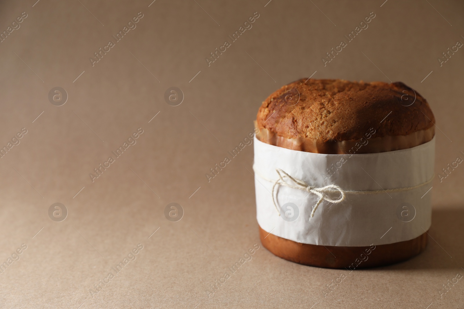 Photo of Delicious Panettone cake wrapped in parchment paper on light brown background, space for text. Traditional Italian pastry