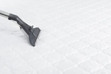 Photo of Using modern vacuum cleaner for mattress disinfection, closeup. Space for text