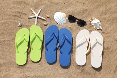 Photo of Stylish colorful flip flops, sunglasses, seashells and starfish on sand outdoors, flat lay