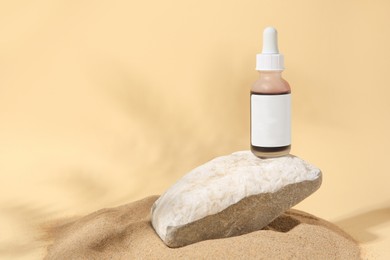 Photo of Bottle of serum and stone on sand against beige background. Space for text