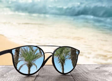Palms mirroring in sunglasses on wooden desk at sandy beach near ocean 