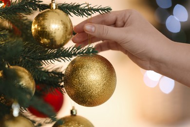 Photo of Woman decorating Christmas tree with golden festive ball on light background, closeup