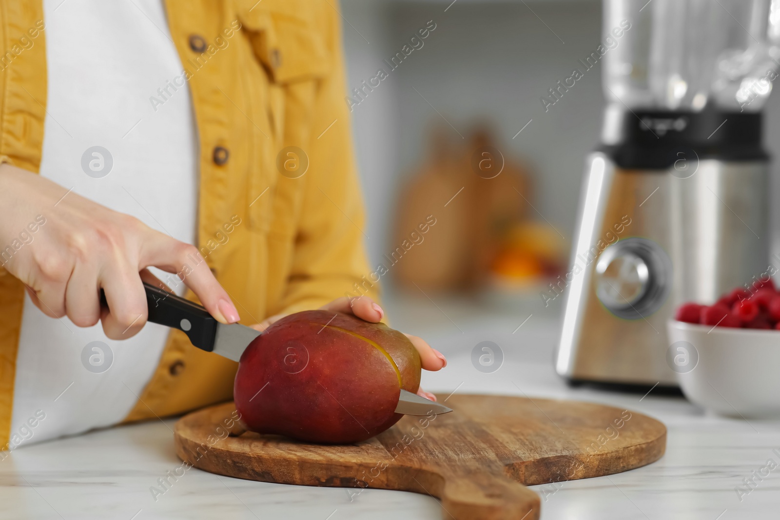 Photo of Woman preparing mango for tasty smoothie at white marble table in kitchen, closeup