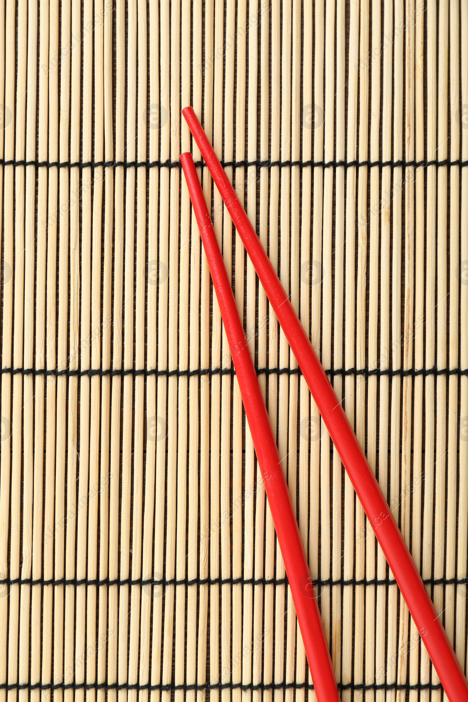 Photo of Pair of red chopsticks on bamboo mat, top view