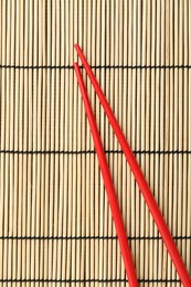 Photo of Pair of red chopsticks on bamboo mat, top view