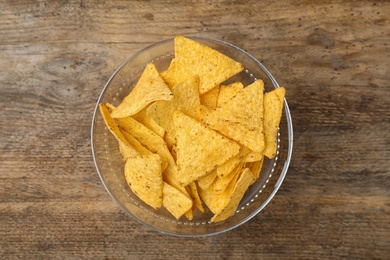 Photo of Glass bowl with tasty Mexican nachos chips on wooden table, top view