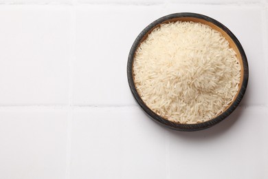 Photo of Raw basmati rice in bowl on white tiled table, top view. Space for text