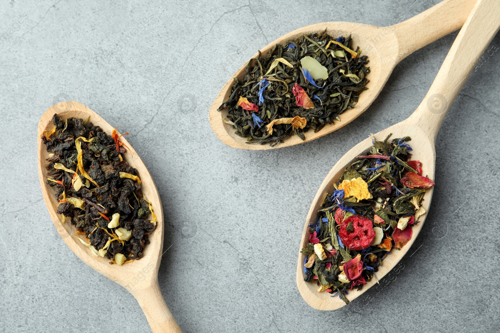 Photo of Different kinds of dry herbal tea in wooden spoons on light grey table, flat lay