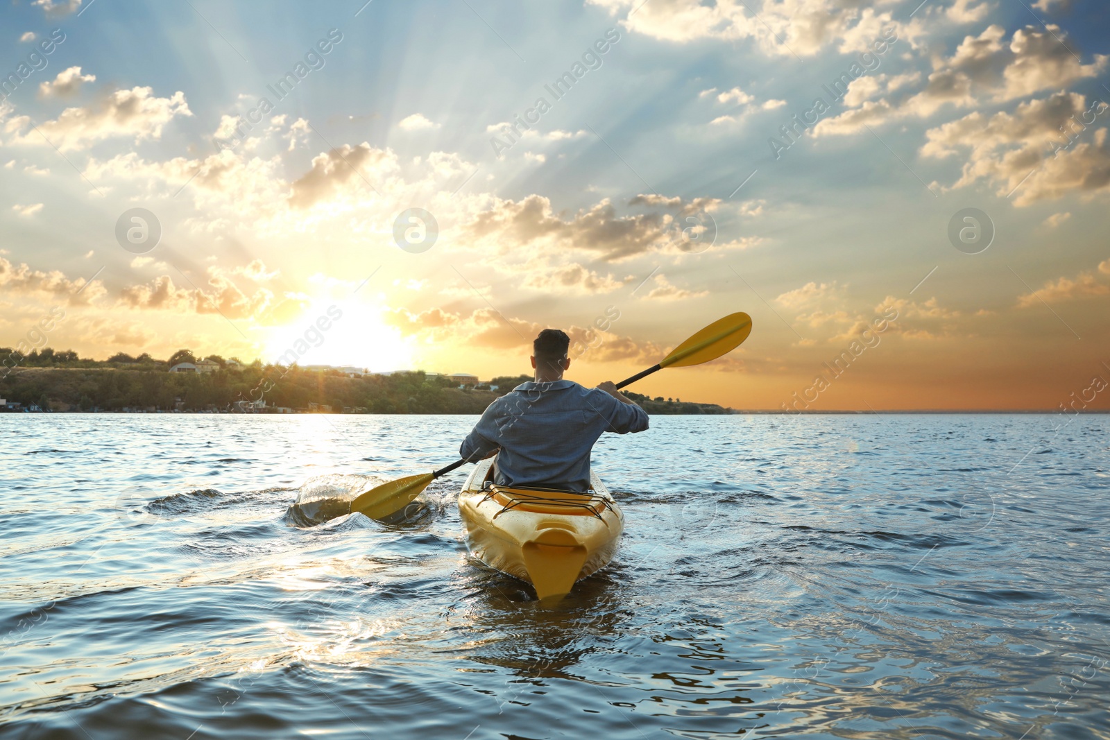 Photo of Man kayaking on river at sunset, back view. Summer activity