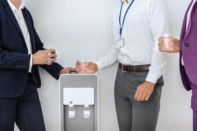 Photo of Co-workers having break near water cooler on white background, closeup