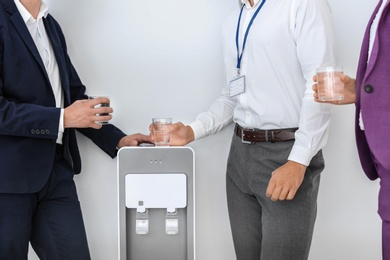 Co-workers having break near water cooler on white background, closeup