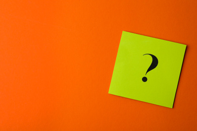 Photo of Green paper card with question mark on orange background, top view. Space for text