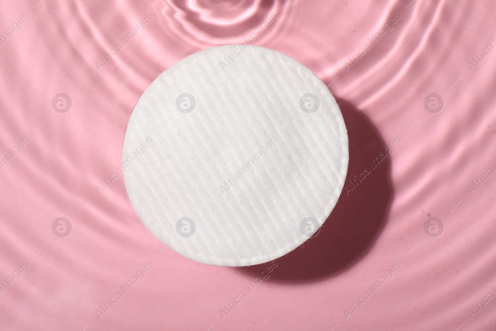 Photo of Cotton pad and micellar water on pink background, top view