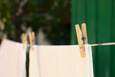 Washing line with clean laundry and clothespins outdoors, closeup. Space for text