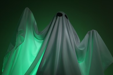 Creepy ghost. Woman covered with sheet in green light, low angle view