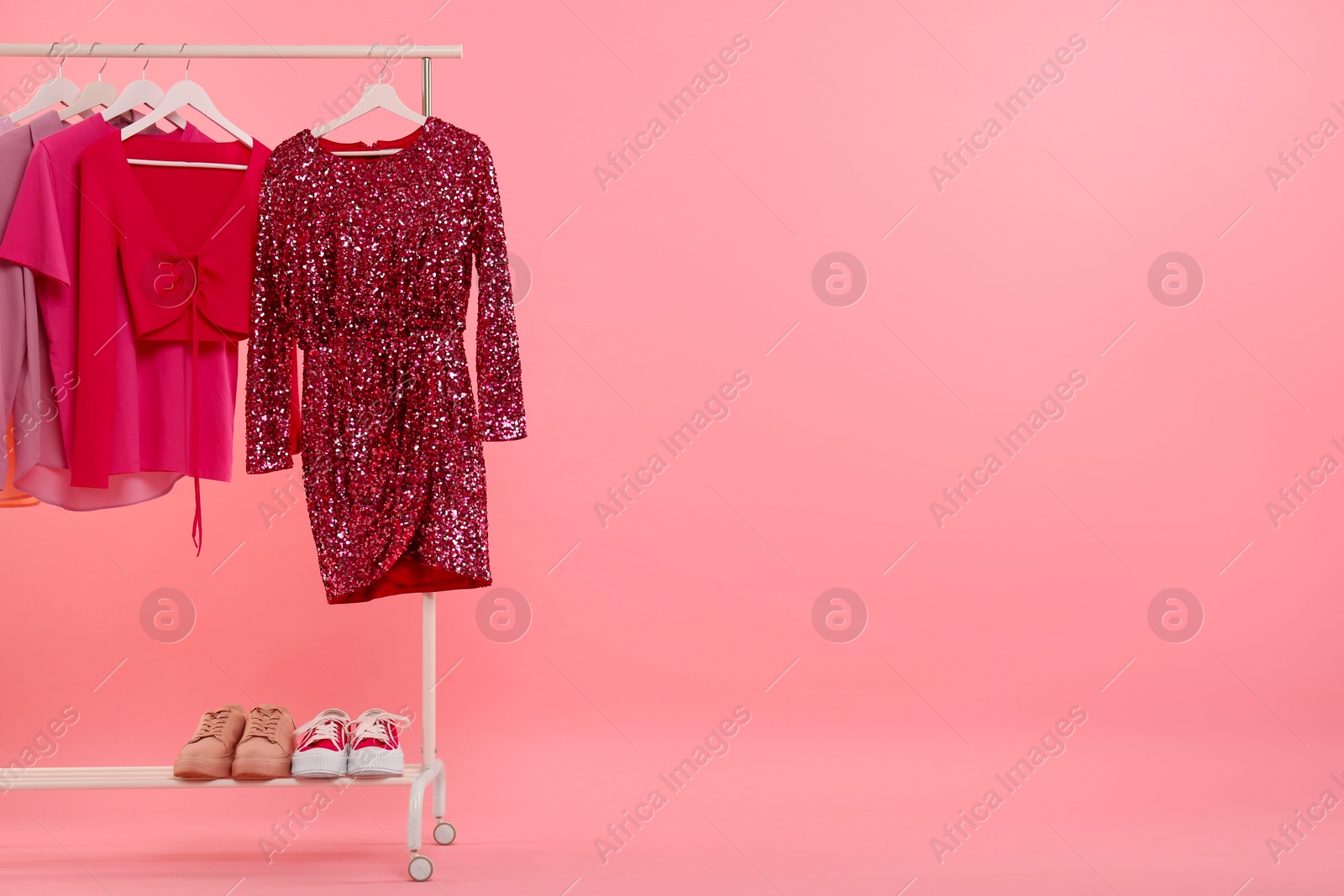 Photo of Rack with different stylish women`s clothes and sneakers on pink background, space for text