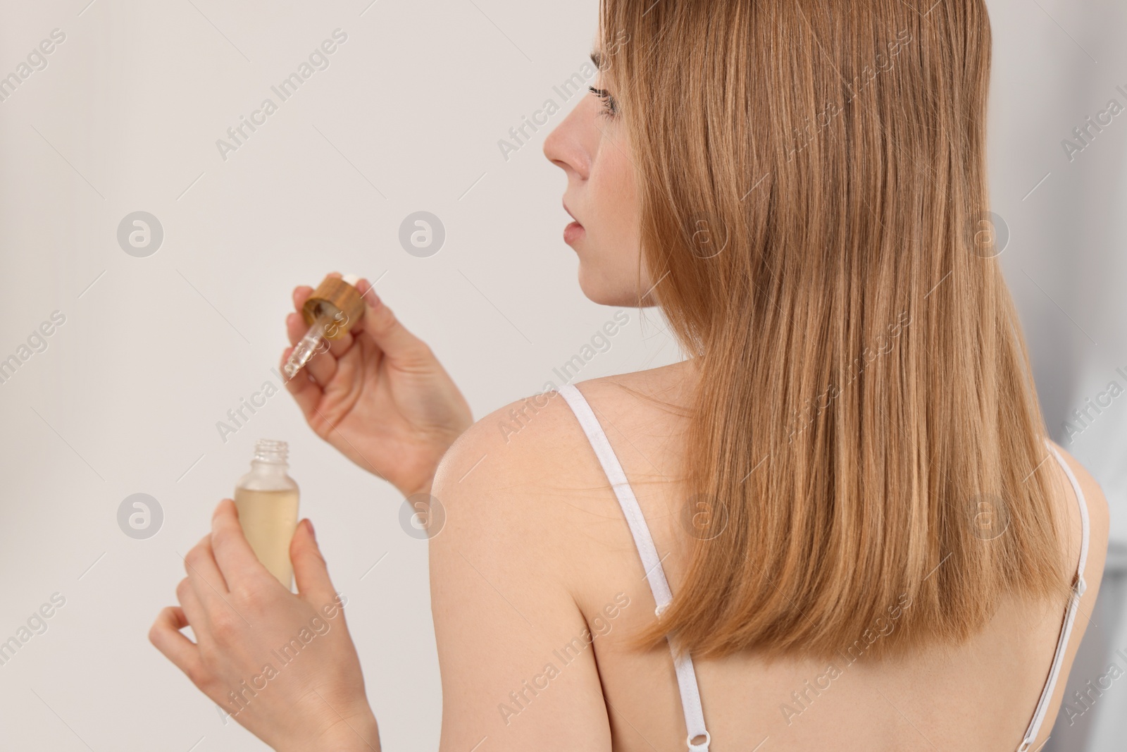 Photo of Woman with bottle of essential oil on blurred background, closeup