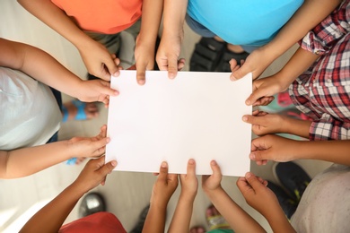 Photo of Little children holding sheet of paper in hands together, top view. Unity concept