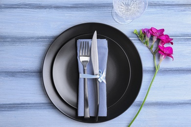 Photo of Stylish elegant table setting with freesia on blue wooden background, top view