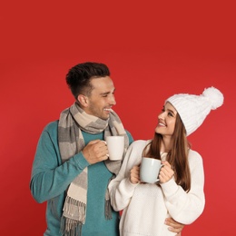 Happy young couple in warm clothes with cups on red background. Winter season