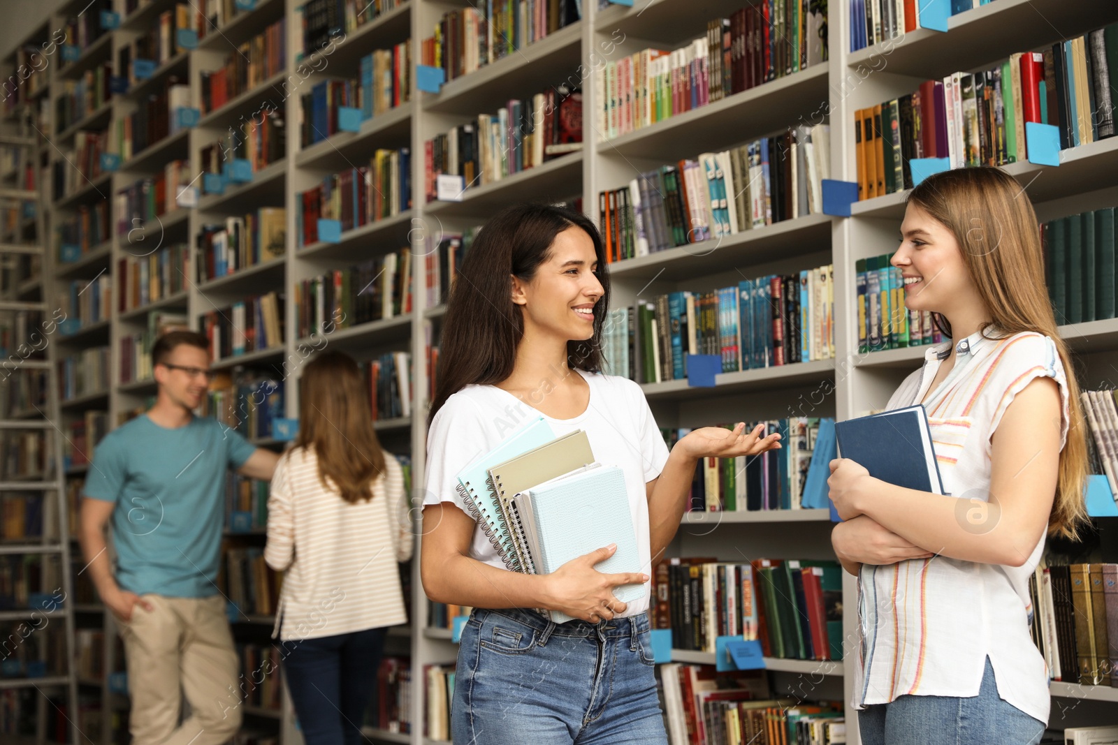 Photo of Young people standing near bookshelves in library